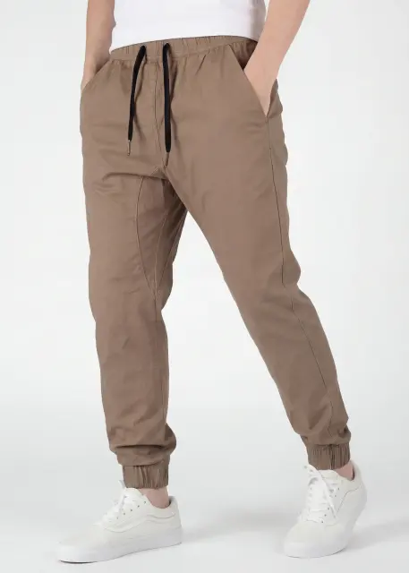  A detailed three-quarter front view of ItalyMorn men's dark khaki jogger pants, emphasizing the relaxed yet tailored fit and the smooth drape of the fabric. A model with hands in pockets against a plain background, wearing white sneakers.