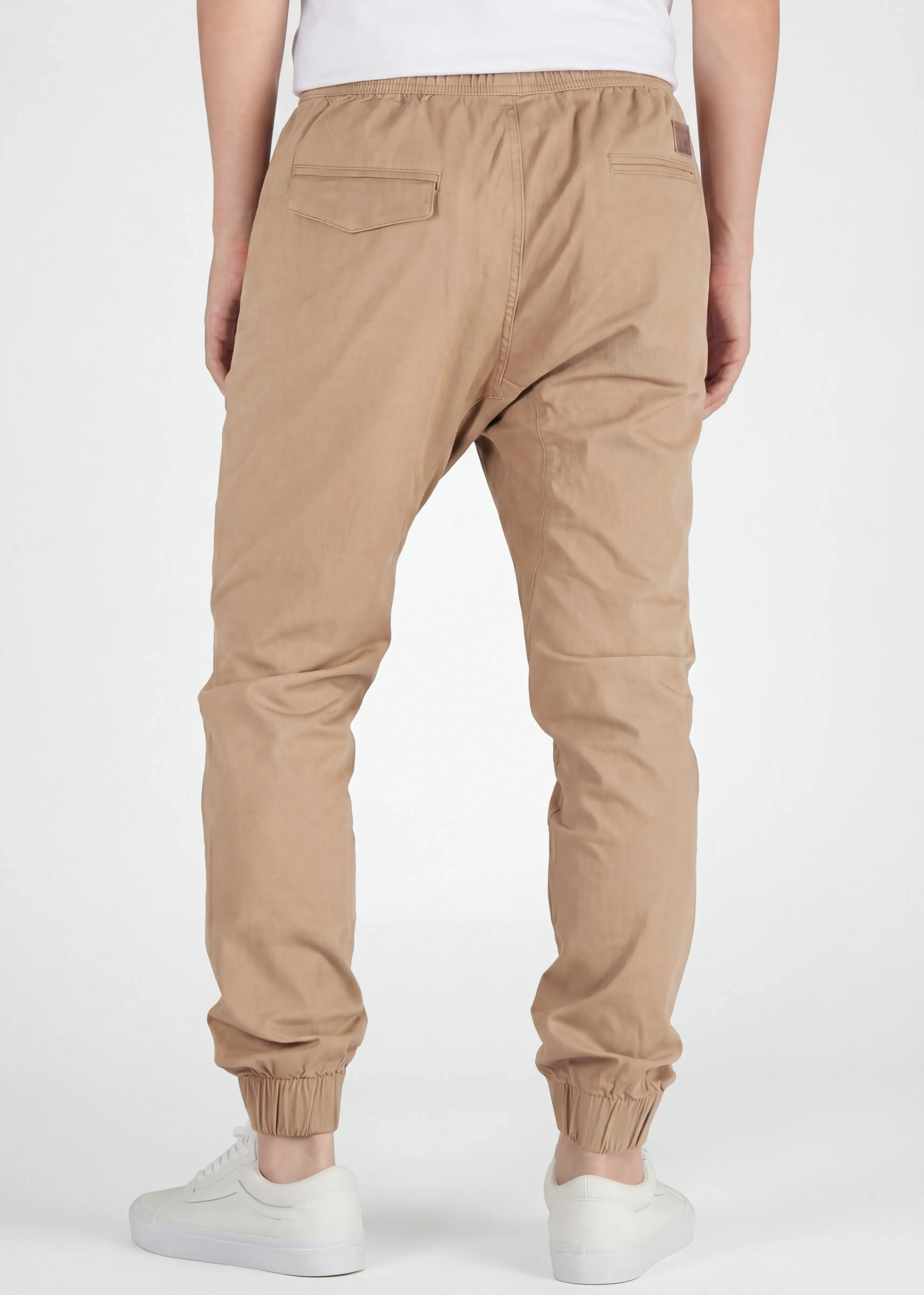 A rear view close-up of ItalyMorn men's khaki jogger pants on a model, highlighting the functional back pockets, clean fit, and durable fabric texture. Paired with white sneakers.