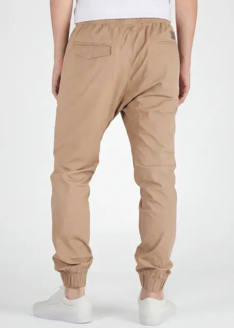 A rear view close-up of ItalyMorn men's khaki jogger pants on a model, highlighting the functional back pockets, clean fit, and durable fabric texture. Paired with white sneakers.