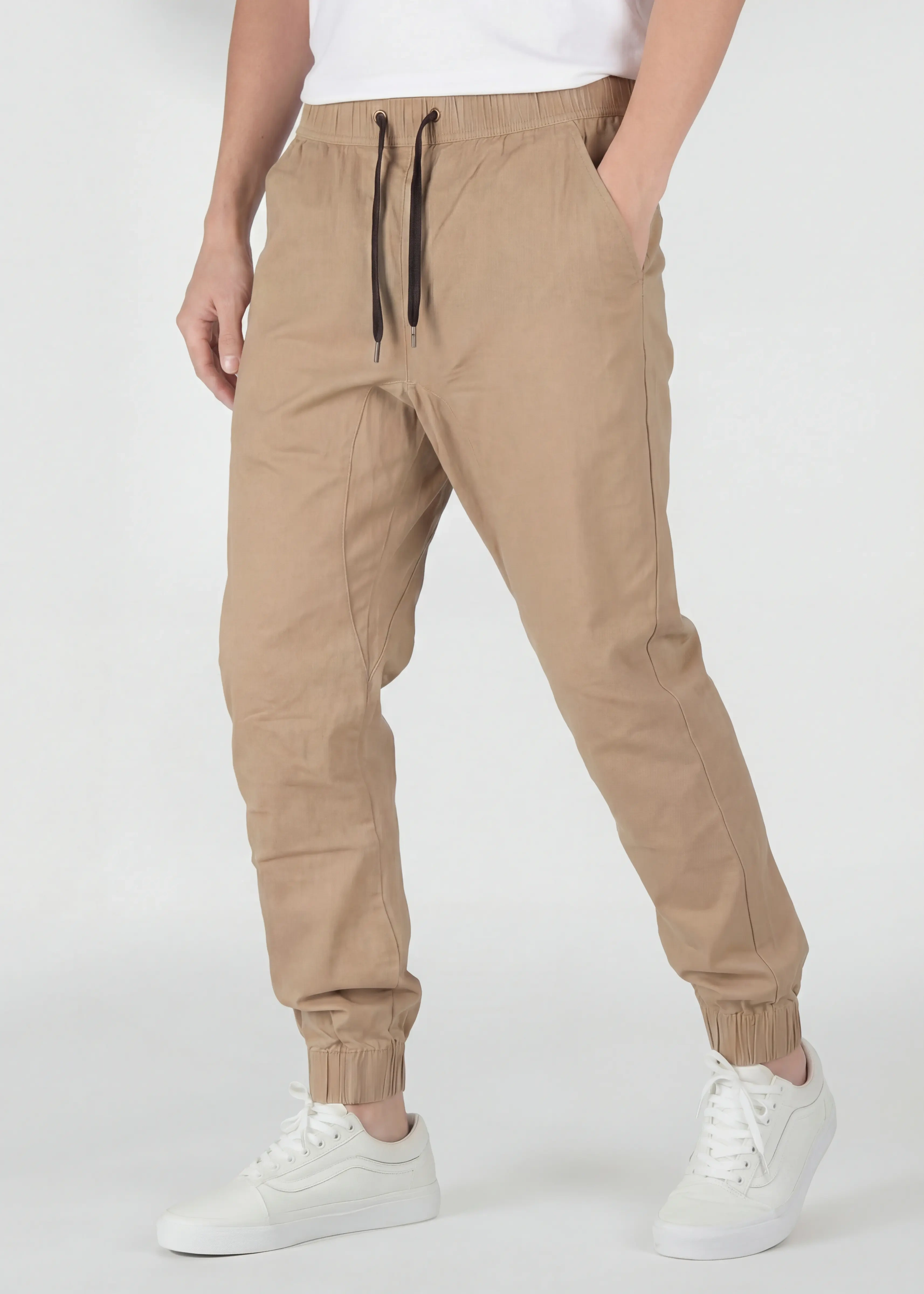 A detailed three-quarter front view of ItalyMorn men's khaki jogger pants, emphasizing the relaxed yet tailored fit and the smooth drape of the fabric. A model with hands in pockets against a plain background, wearing white sneakers.