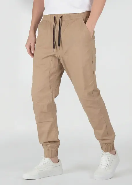 A detailed three-quarter front view of ItalyMorn men's khaki jogger pants, emphasizing the relaxed yet tailored fit and the smooth drape of the fabric. A model with hands in pockets against a plain background, wearing white sneakers.