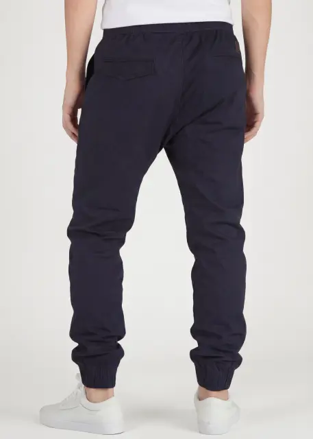  Back view of ItalyMorn men's navy blue jogger pants on a model, showing the clean tailored fit, functional back pockets, and snug ribbed ankle cuffs
