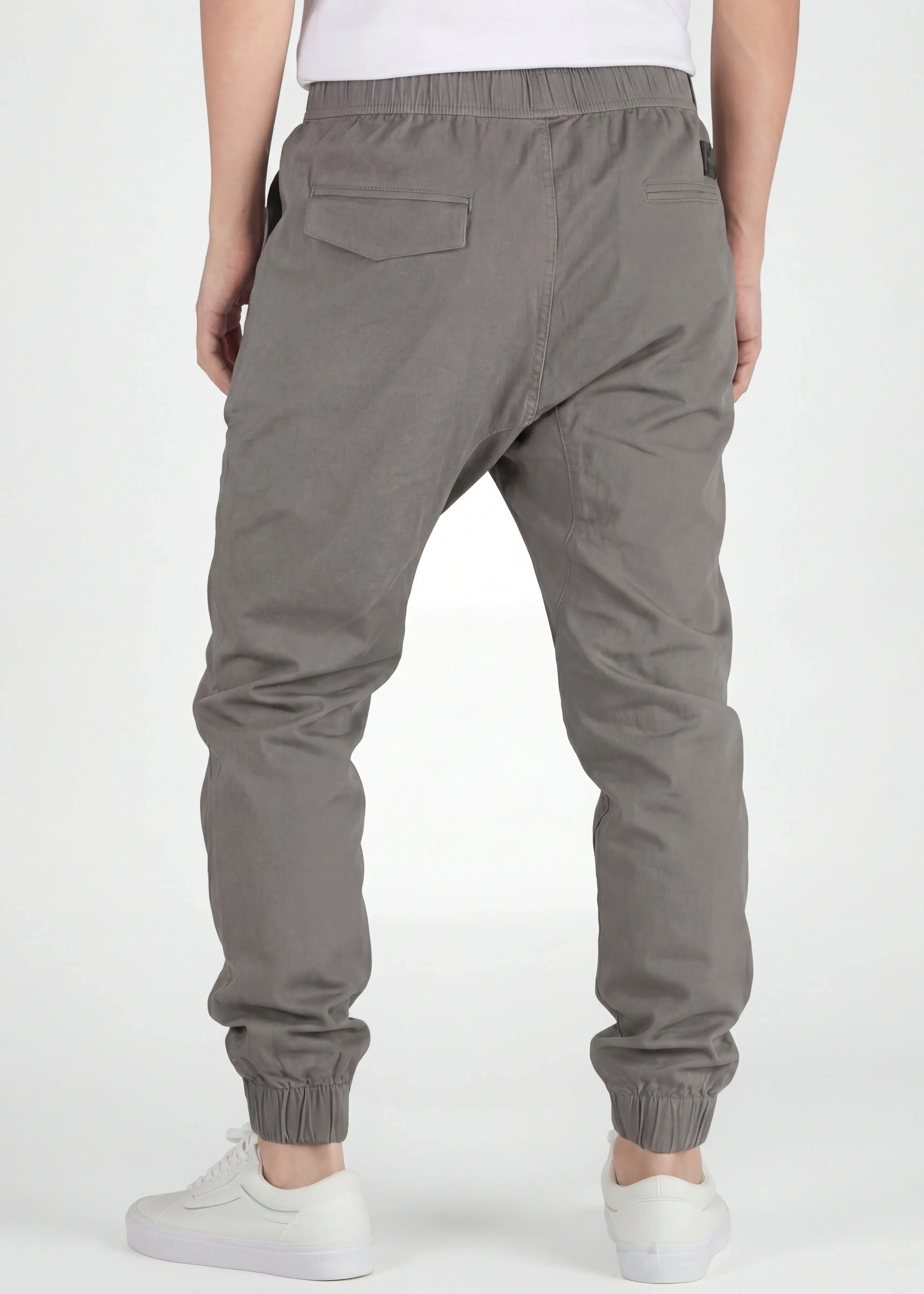 A rear view close-up of ItalyMorn men's mid grey jogger pants on a model, highlighting the functional back pockets, clean fit, and durable fabric texture. Paired with white sneakers