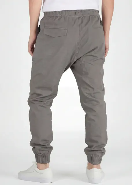 A rear view close-up of ItalyMorn men's mid grey jogger pants on a model, highlighting the functional back pockets, clean fit, and durable fabric texture. Paired with white sneakers