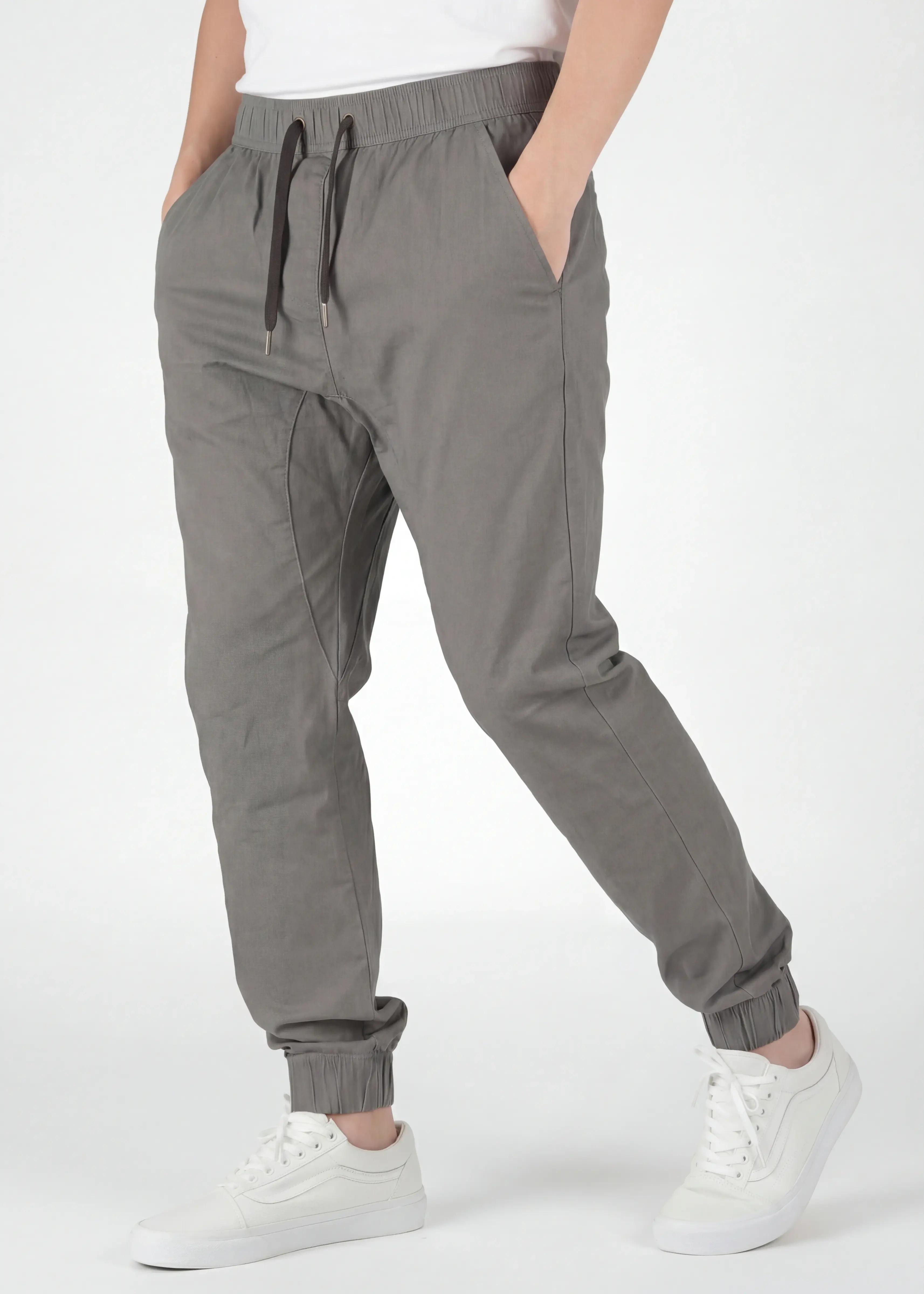 A detailed three-quarter front view of ItalyMorn men's mid grey jogger pants, emphasizing the relaxed yet tailored fit and the smooth drape of the fabric. A model with hands in pockets against a plain background, wearing white sneakers