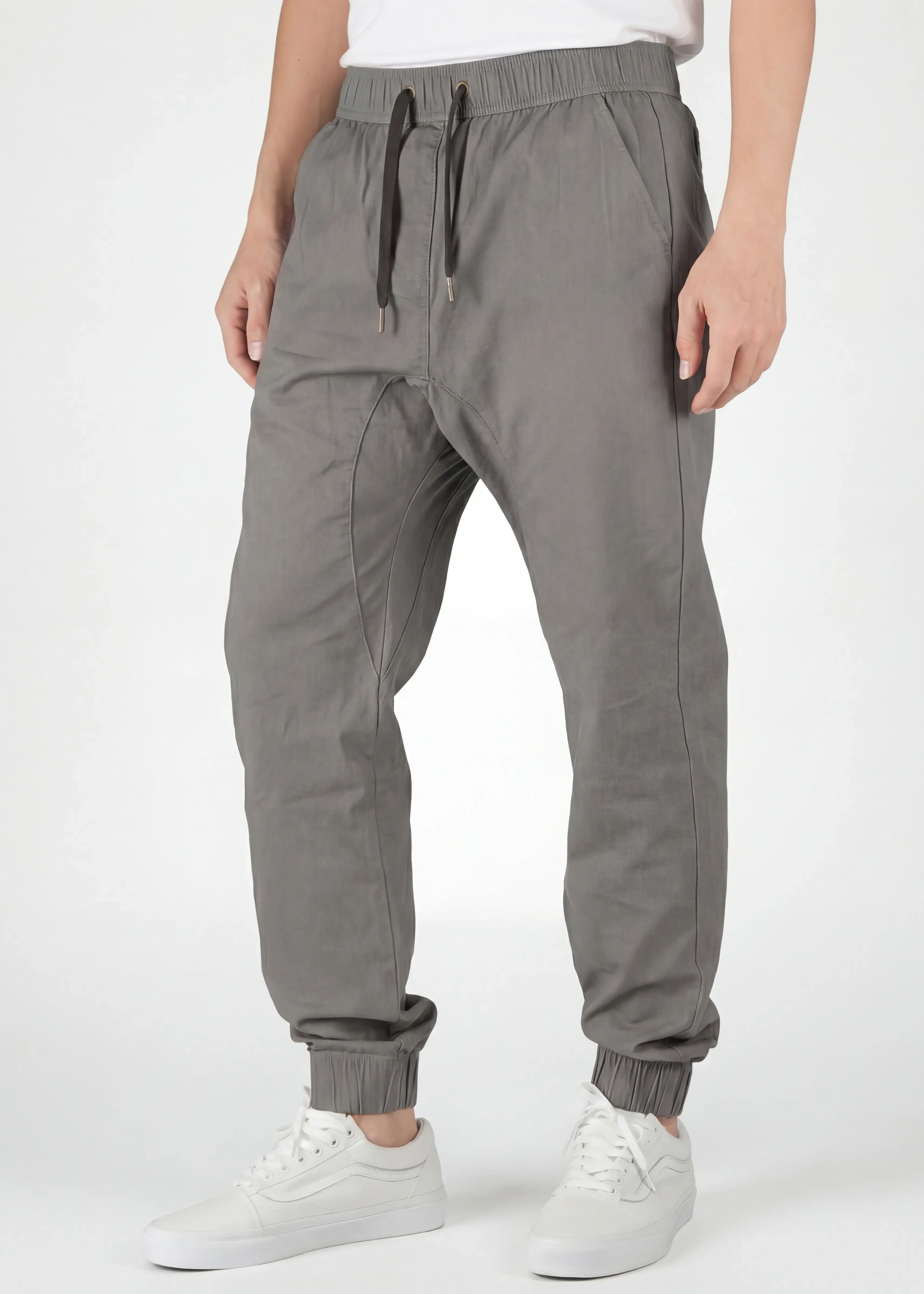A detailed close-up view from the front of ItalyMorn men's mid grey jogger pants, showcasing the elastic waistband with drawstrings, practical front pockets, and ribbed cuffs. A model's lower body is shown, wearing white sneakers