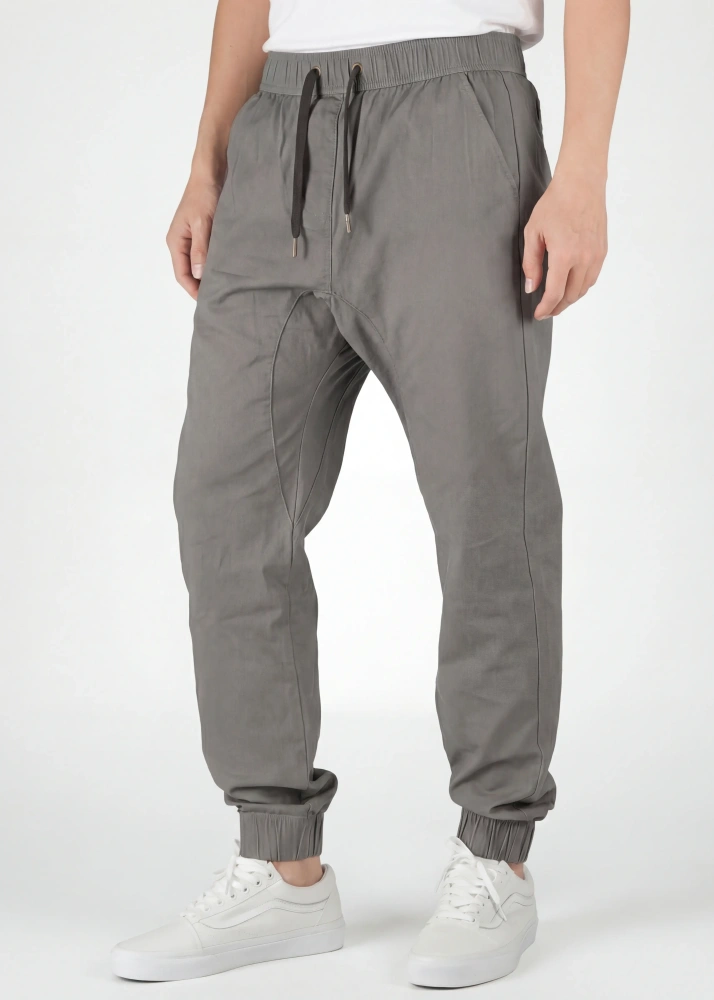 A detailed close-up view from the front of ItalyMorn men's mid grey jogger pants, showcasing the elastic waistband with drawstrings, practical front pockets, and ribbed cuffs. A model's lower body is shown, wearing white sneakers