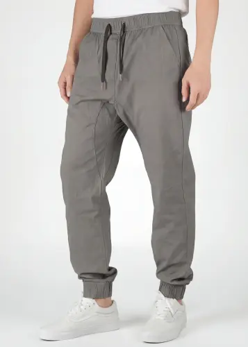 A detailed close-up view from the front of ItalyMorn men's mid grey jogger pants, showcasing the elastic waistband with drawstrings, practical front pockets, and ribbed cuffs. A model's lower body is shown, wearing white sneakers