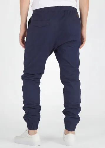A rear close-up view of ItalyMorn men's navy blue jogger pants, showcasing the clean tailored fit, functional back pockets with flap detail, and secure ribbed ankle cuffs. Paired with white sneakers.
