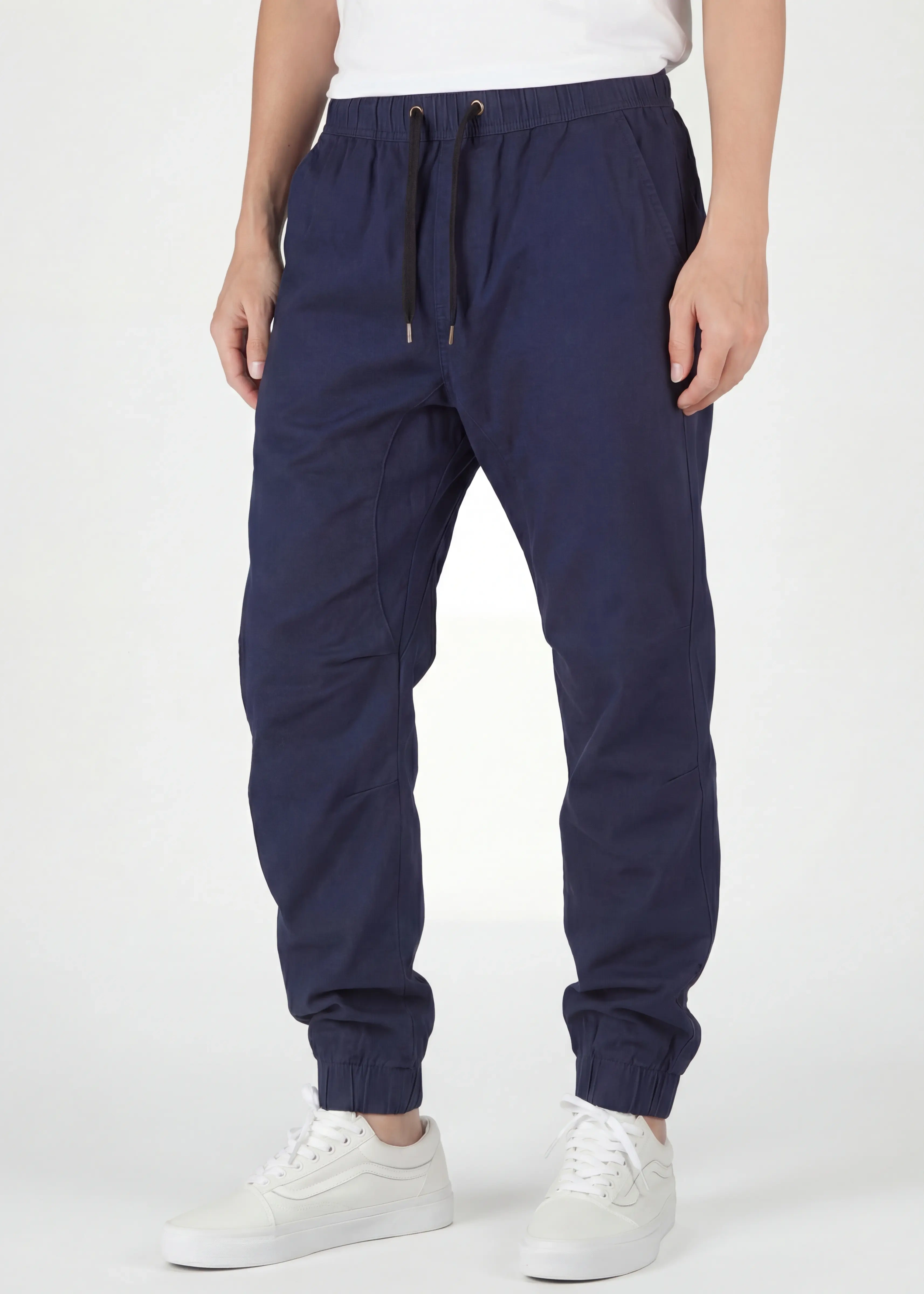  A close-up front view of ItalyMorn men's navy blue jogger pants on a model, highlighting the comfortable elastic waistband with black drawstrings, deep side pockets, and slim-tapered silhouette. Paired with white sneakers