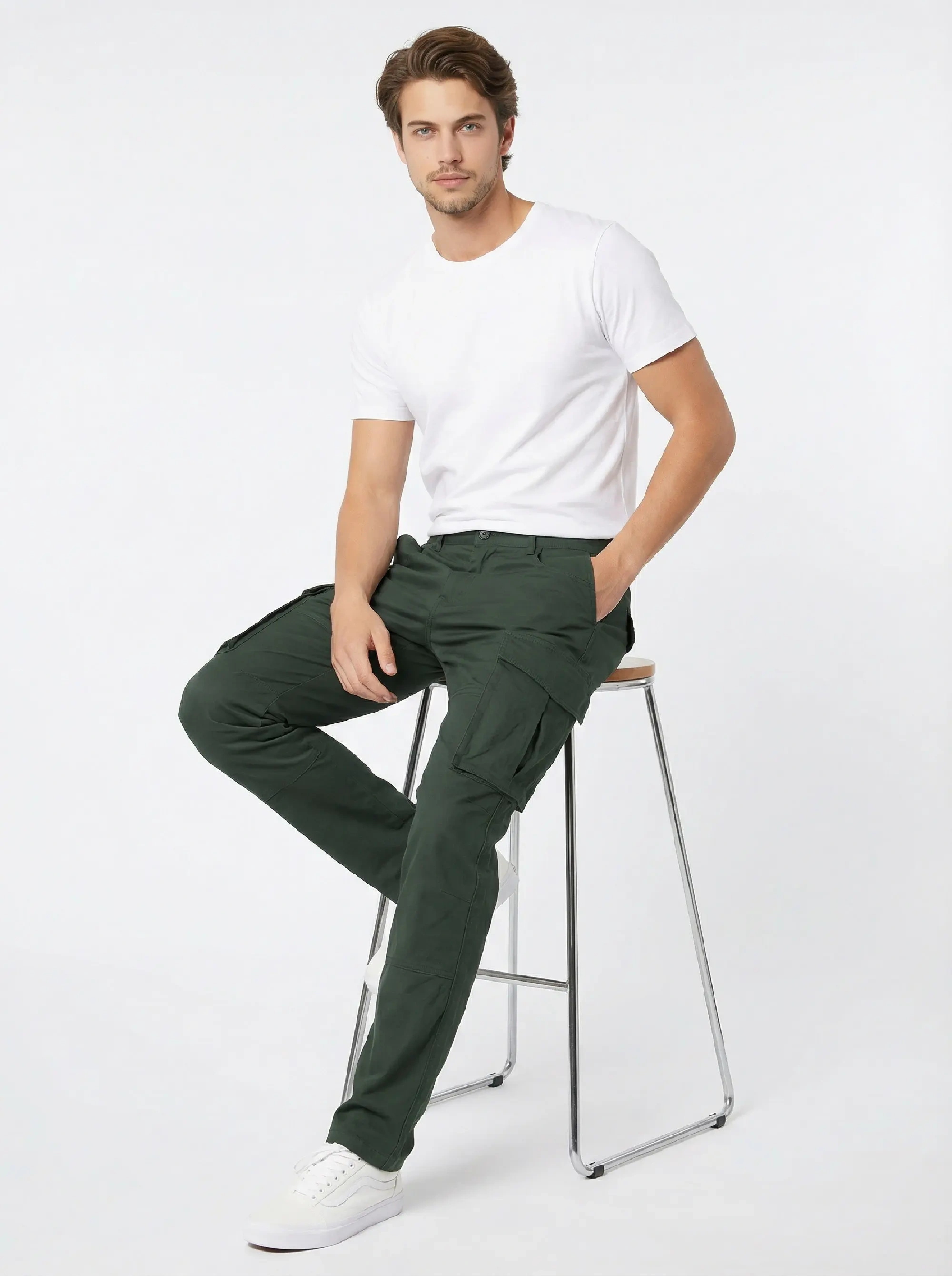 A male model sitting on a modern stool wearing a white t-shirt and ItalyMorn men's army green cargo pants, demonstrating the comfortable fit and flexibility of the pants when seated.