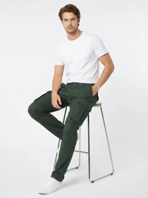 A male model sitting on a modern stool wearing a white t-shirt and ItalyMorn men's army green cargo pants, demonstrating the comfortable fit and flexibility of the pants when seated.