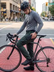A man pausing on his road bike at a city intersection, easily pulling his smartphone from the side pocket of his ItalyMorn men's army green cargo pants, highlighting excellent urban utility and convenience.