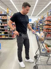 A man grocery shopping with a cart, conveniently putting his wallet into the front pocket of his ItalyMorn men's dark grey cargo pants, highlighting practical utility and comfort for everyday errands.