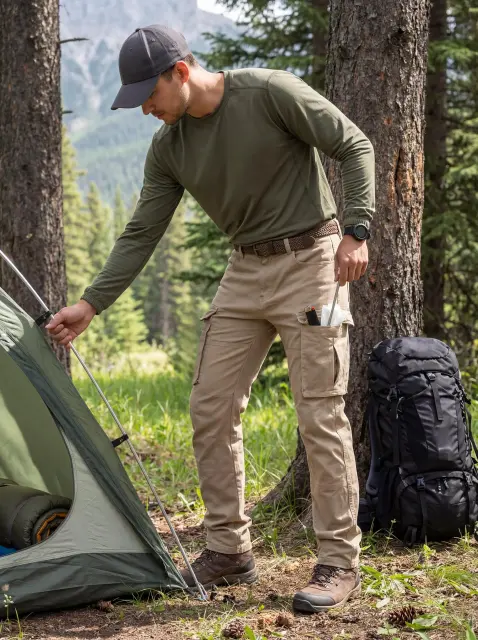 A man setting up a camping tent in the forest, easily accessing tent pegs from the functional side cargo pocket of his ItalyMorn men's khaki cargo pants, highlighting rugged outdoor durability.