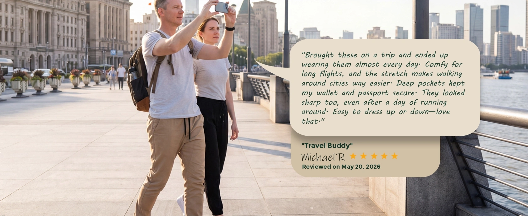 A man taking a photo with his phone while walking along a city waterfront wearing ItalyMorn khaki classic joggers. A customer review overlay praises the pants as an ideal travel buddy for long flights and walking around cities.