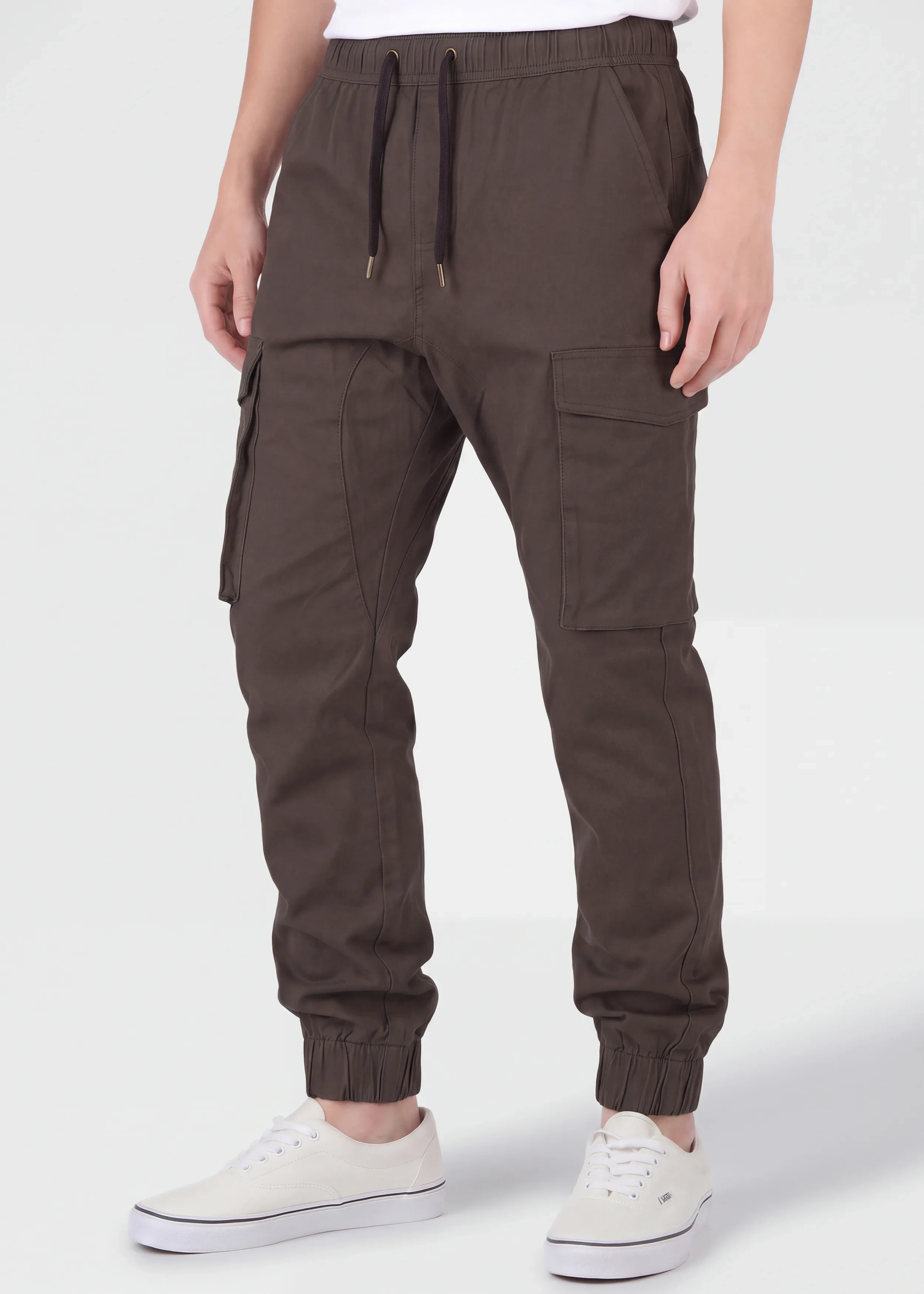 Front view of a male model wearing ITALYMORN men's dark brown cargo joggers, featuring an elastic waistband with black drawstrings, side cargo pockets, and ankle cuffs, paired with a white t-shirt and white sneakers.