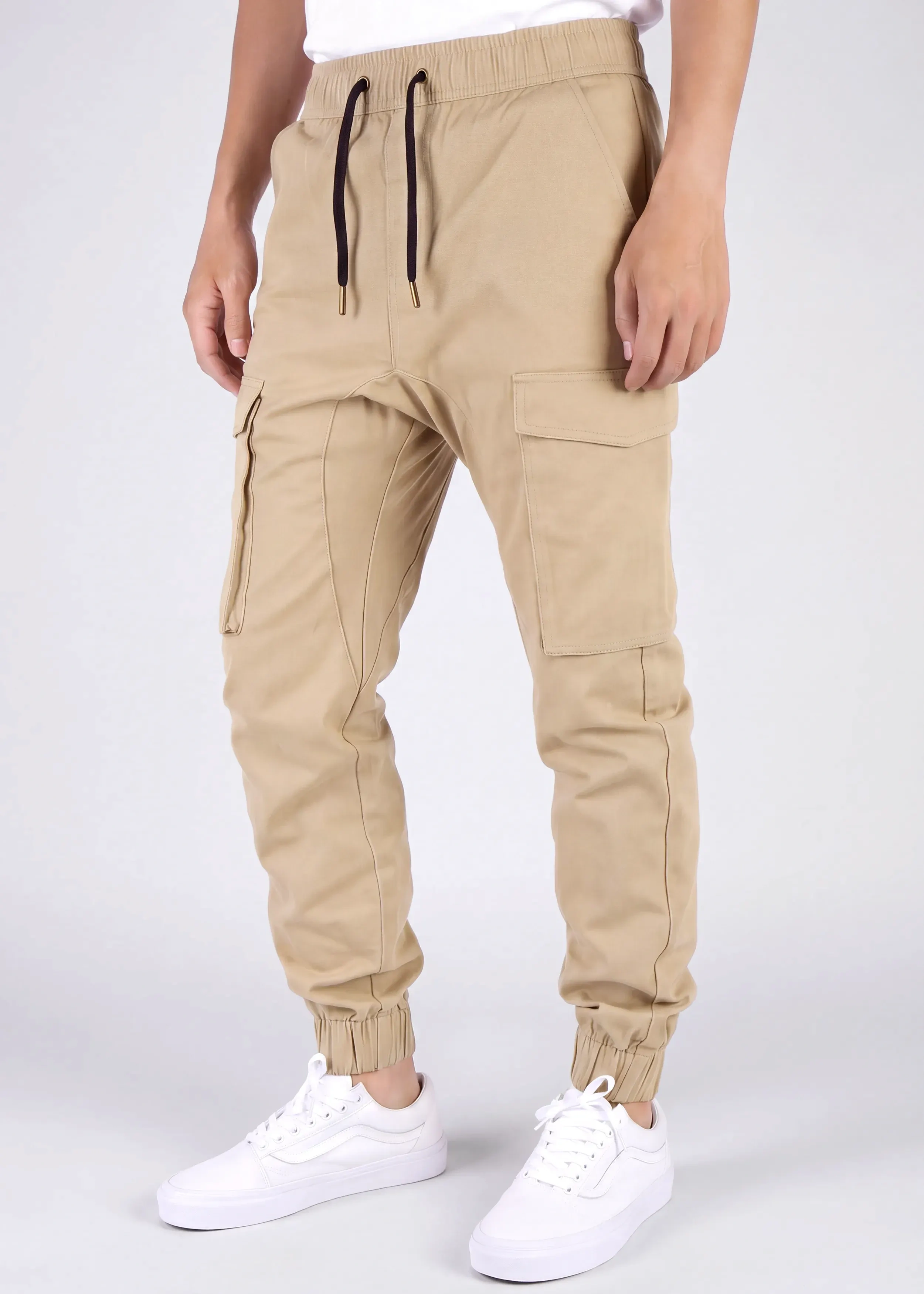 Front view of a male model wearing ITALYMORN men's khaki cargo joggers, featuring an elastic waistband with black drawstrings, side cargo pockets, and ankle cuffs, paired with a white t-shirt and white sneakers.