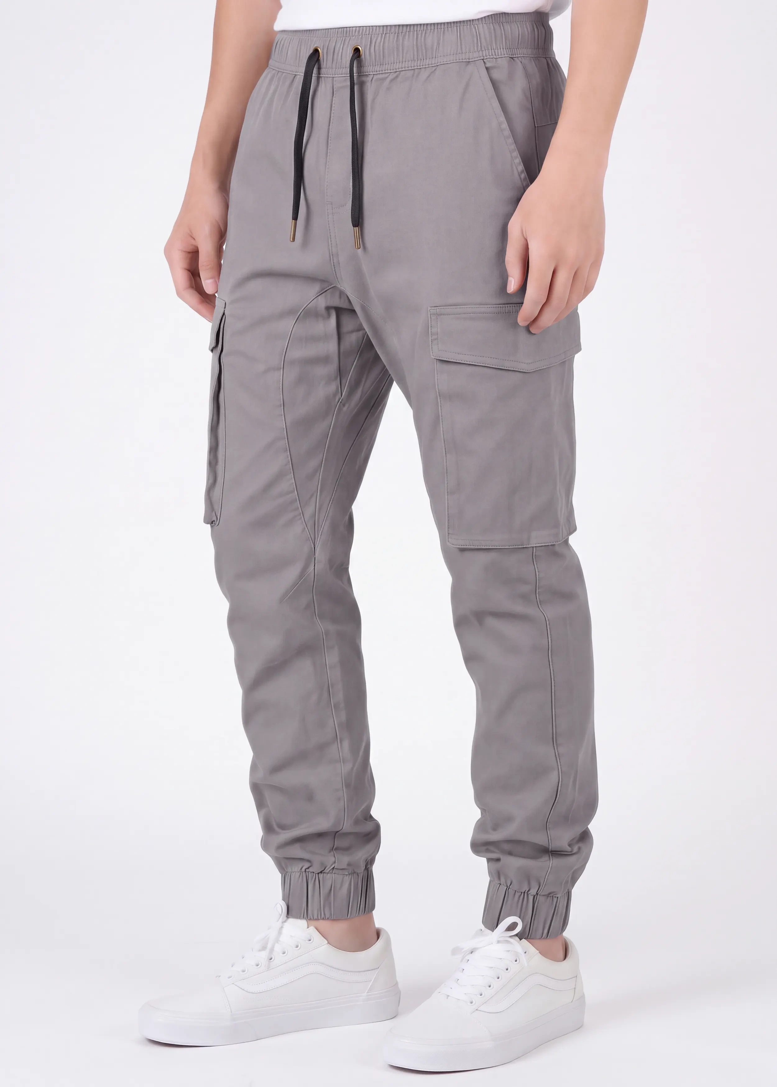 Front view of a male model wearing ITALYMORN men's mid grey cargo joggers, featuring an elastic waistband with black drawstrings, side cargo pockets, and ankle cuffs, paired with a white t-shirt and white sneakers.
