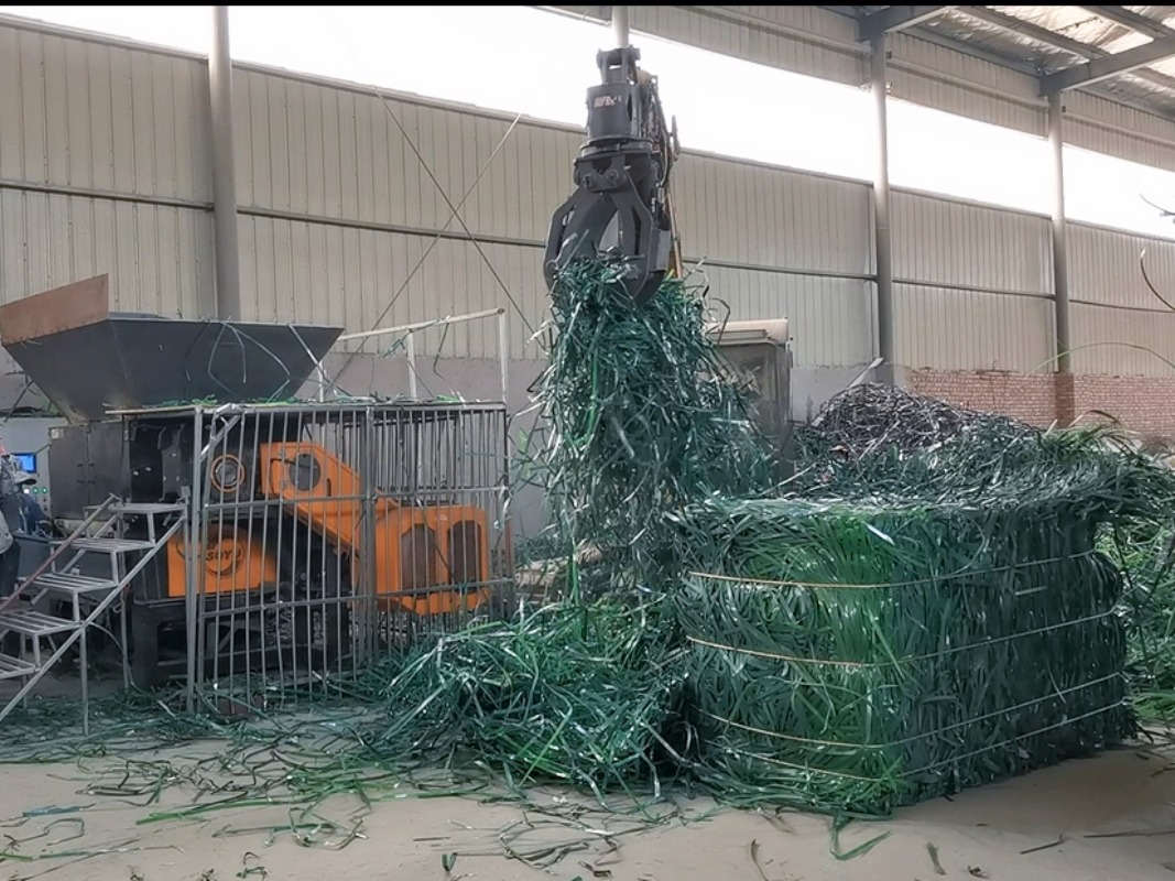 A grab crane feeding compressed green plastic strapping bands and packaging straps into the SOYU shredder.