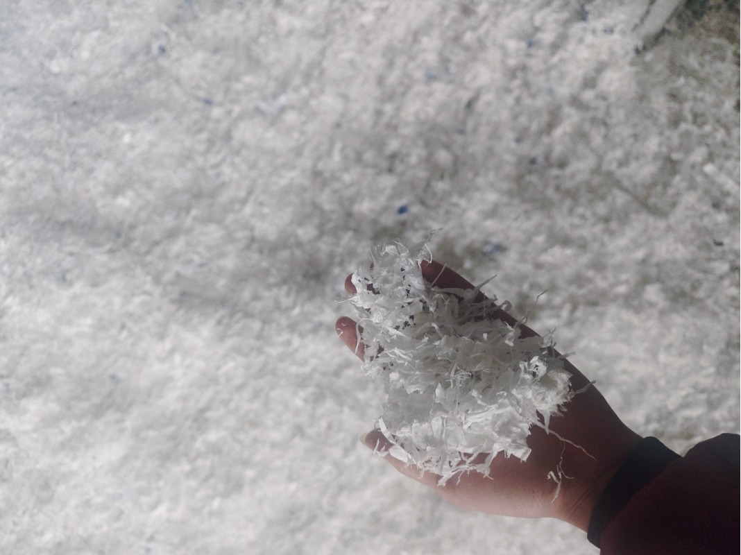 Hand-holding display of high-quality uniform white plastic film flakes processed by SOYU shredder machine.