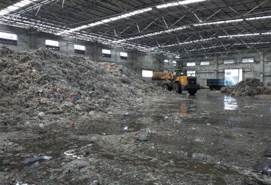 Massive piles of scrap paper mill rejects and light waste being managed by a loader in a large warehouse.