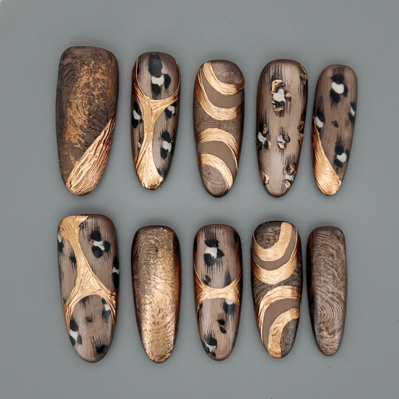 Law of the Wild long oval press-on nails with bronze-brown base, cheetah spots, and gold foil accents with glossy finish