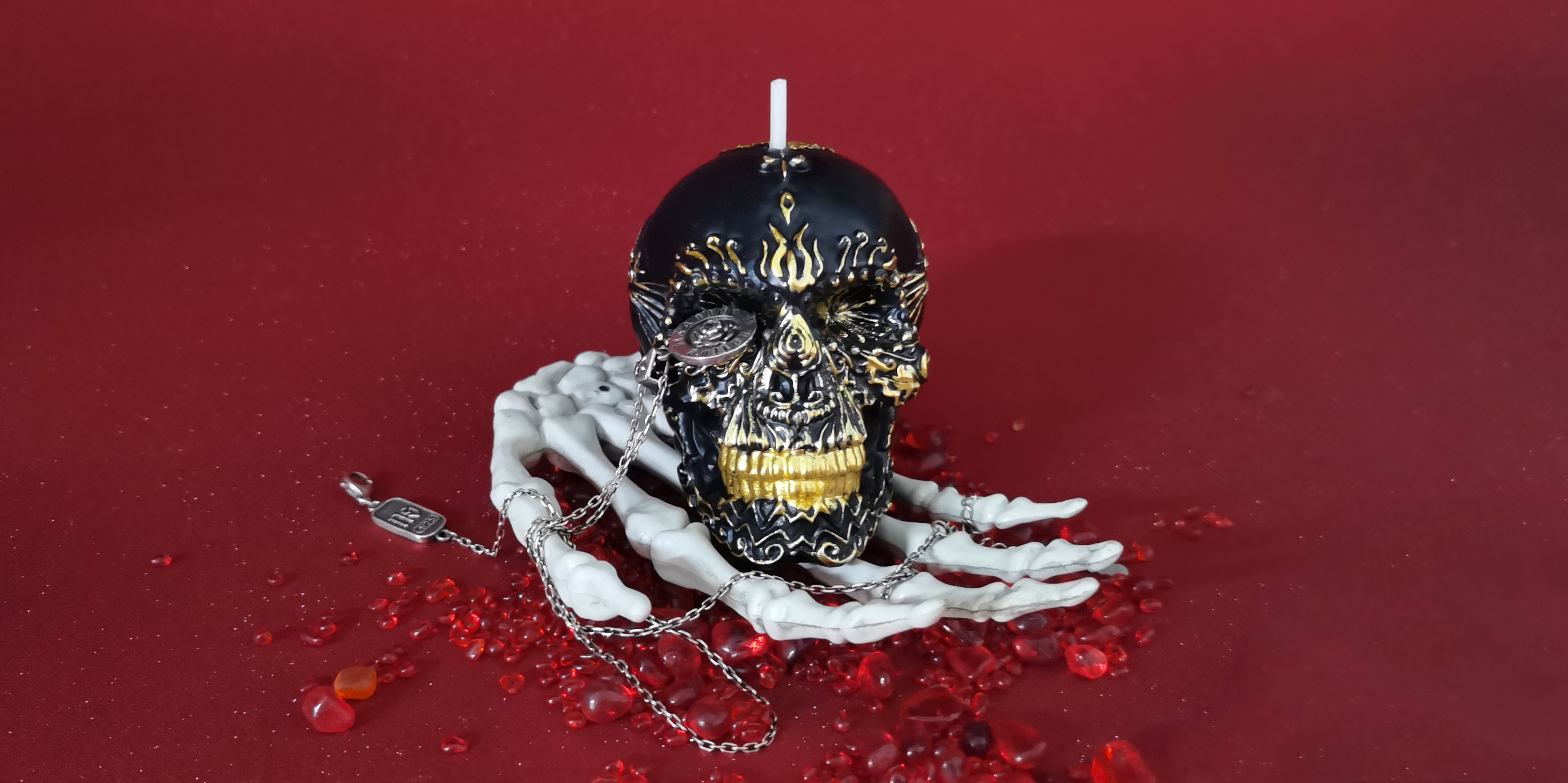 Gilded Black Skull Candle on a skeleton hand with a pendant in one eye_horizontal