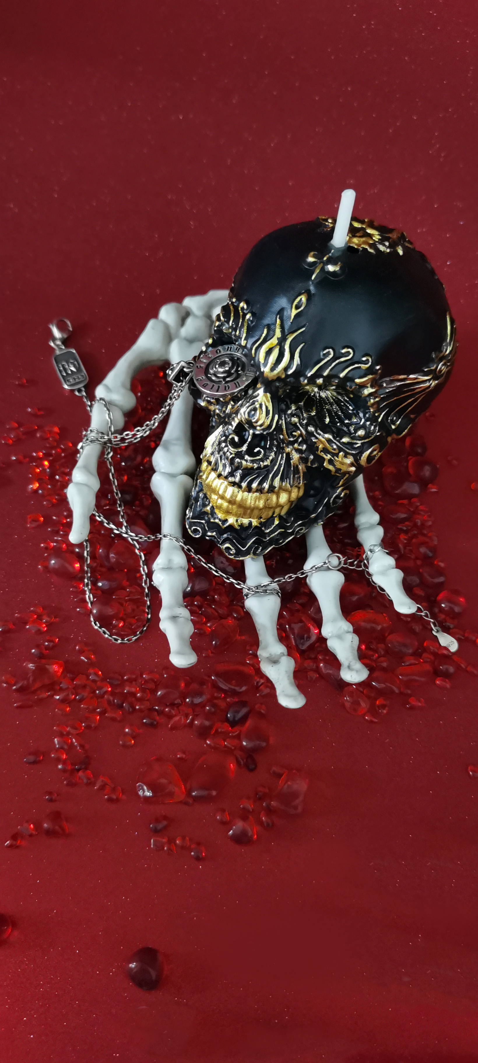 Gilded Black Skull Candle on a skeleton hand with a pendant in one eye_vertical