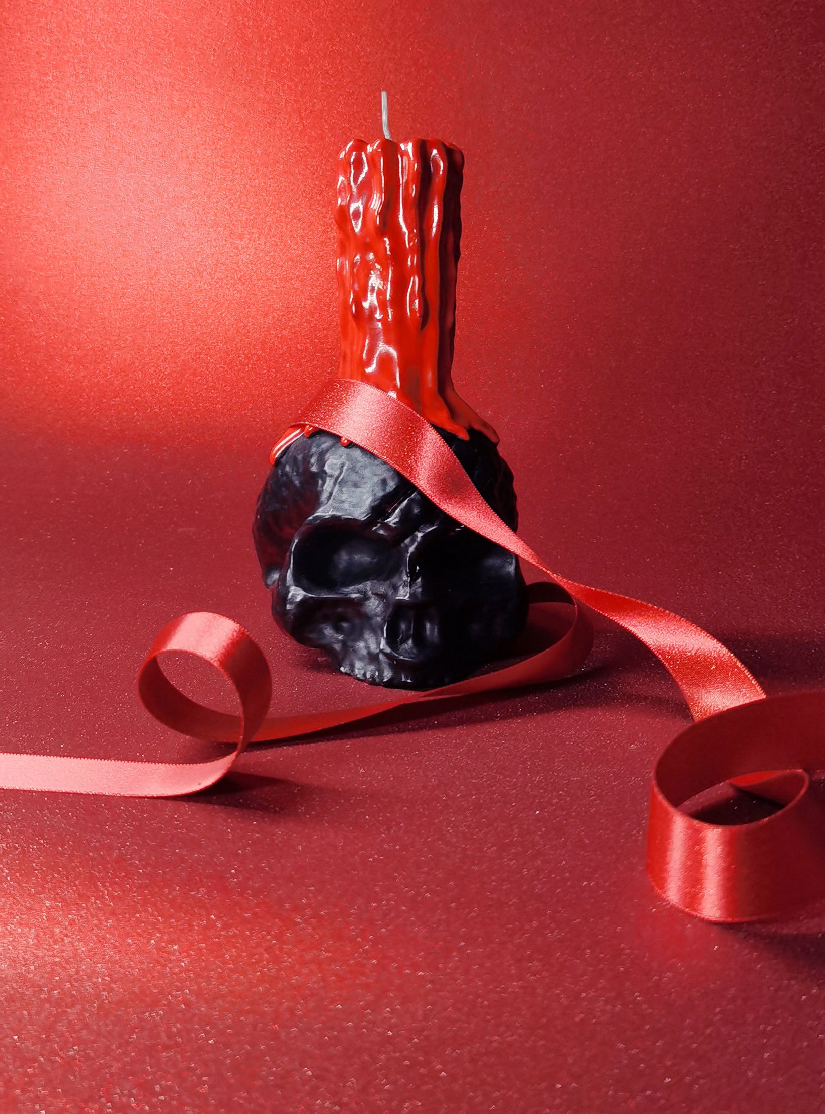 A Red Ribbon Wrapped Around a Gothic Skull Candle with Red Dripping Pillar