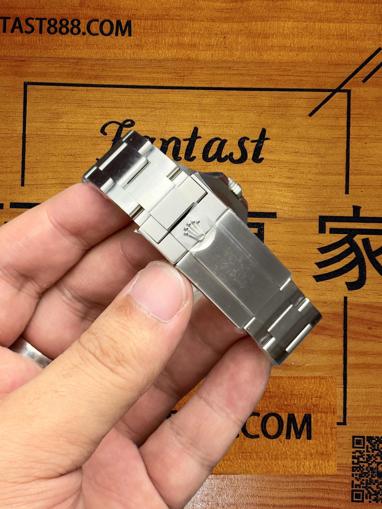 勞力士腕錶側上方視角，清晰顯示錶殼側面Swiss Made印記與白色錶盤數字時標，背景木質板印有TAST888.COM與Fantast字樣。