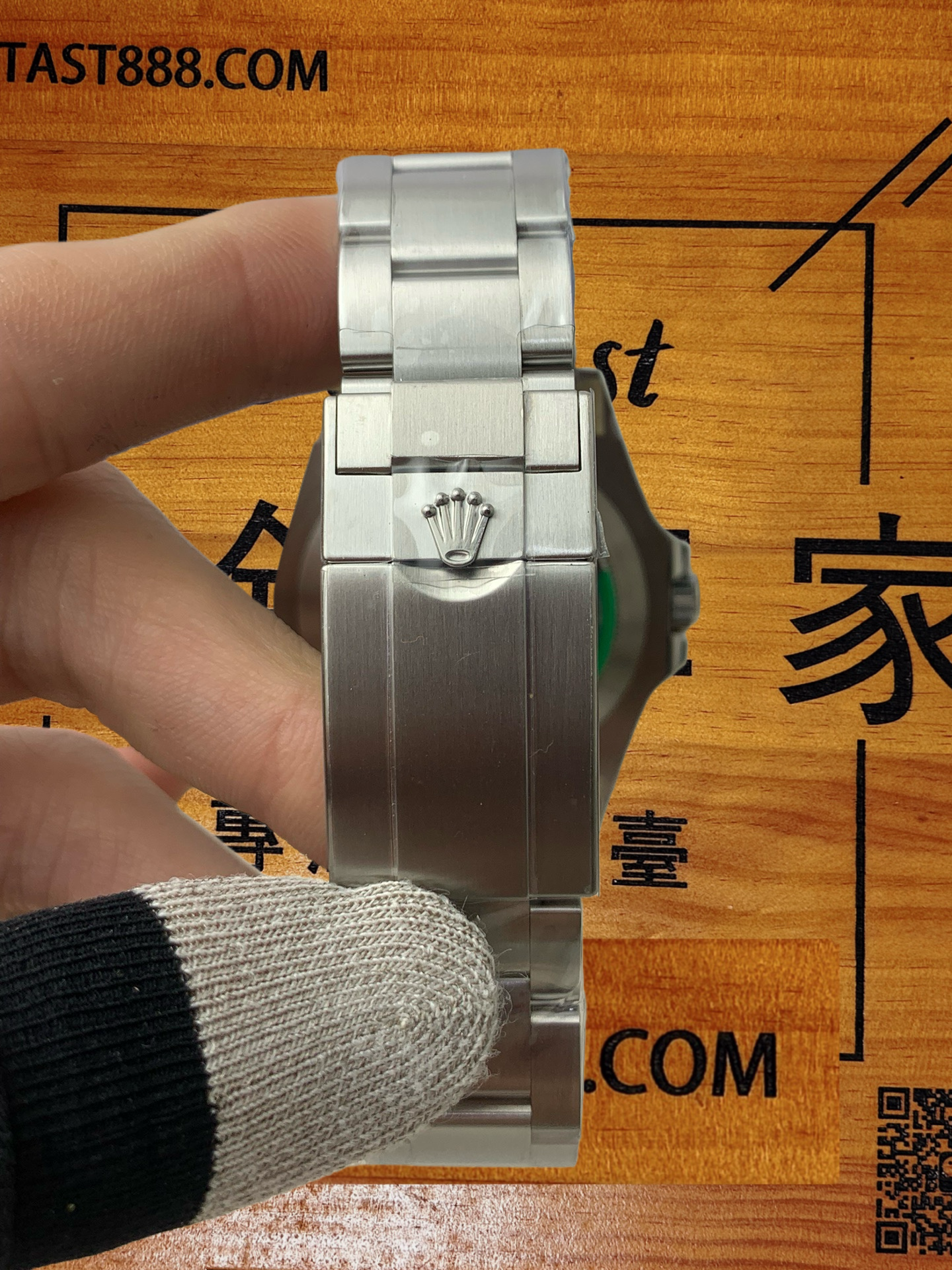 勞力士腕錶錶扣特寫，不鏽鋼錶鏈拉絲工藝細膩，錶扣中央刻有品牌皇冠標誌，手套握持展示，木質背景印有「FANTAST888.COM」及「Fantast」標識。
