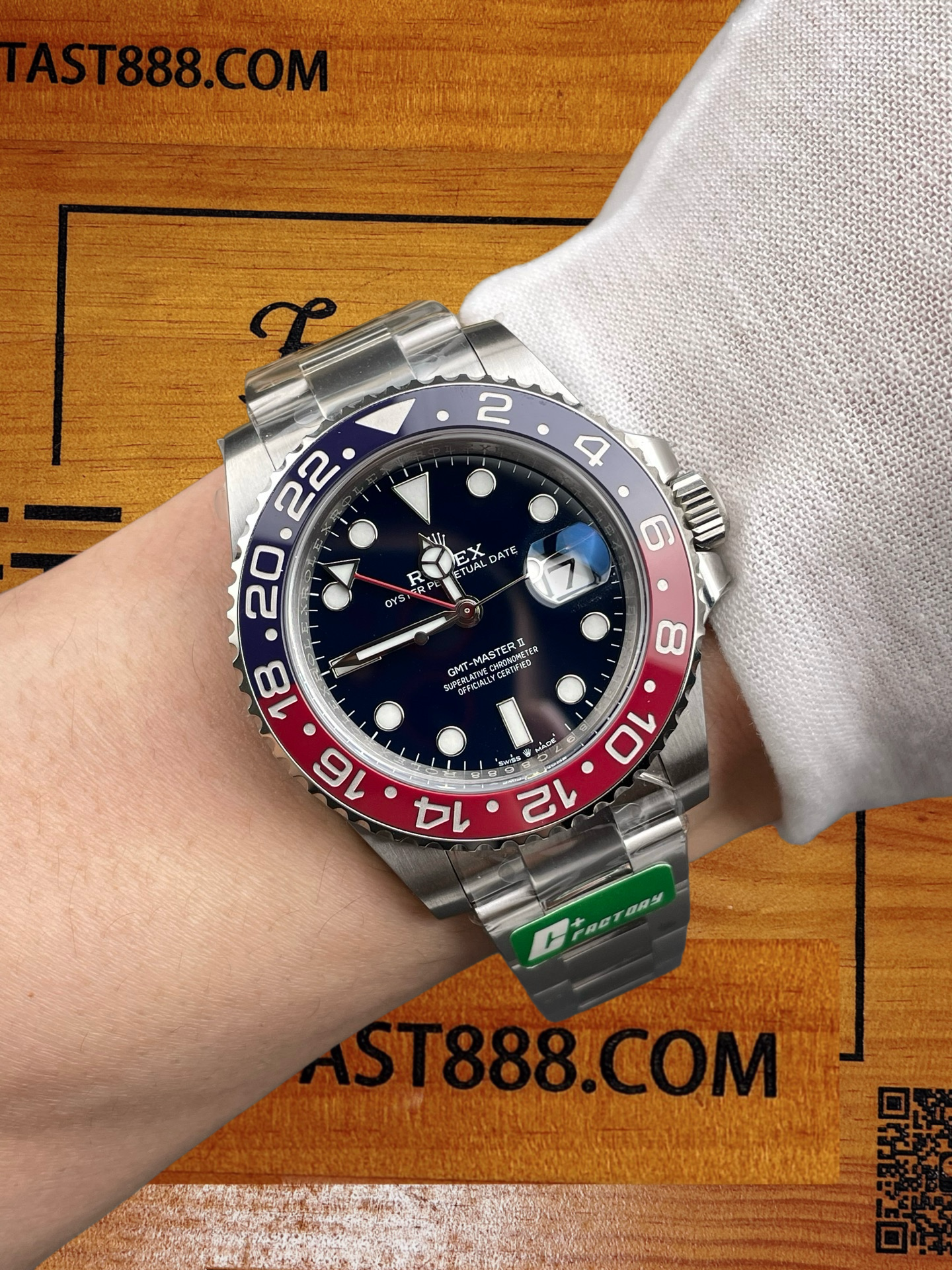 C+廠勞力士可樂圈復刻腕錶佩戴效果實拍，黑色錶盤與紅藍錶圈，綠色C FACTORY標籤懸於錶帶，背景為印有FANTAST888.COM的木質桌面。