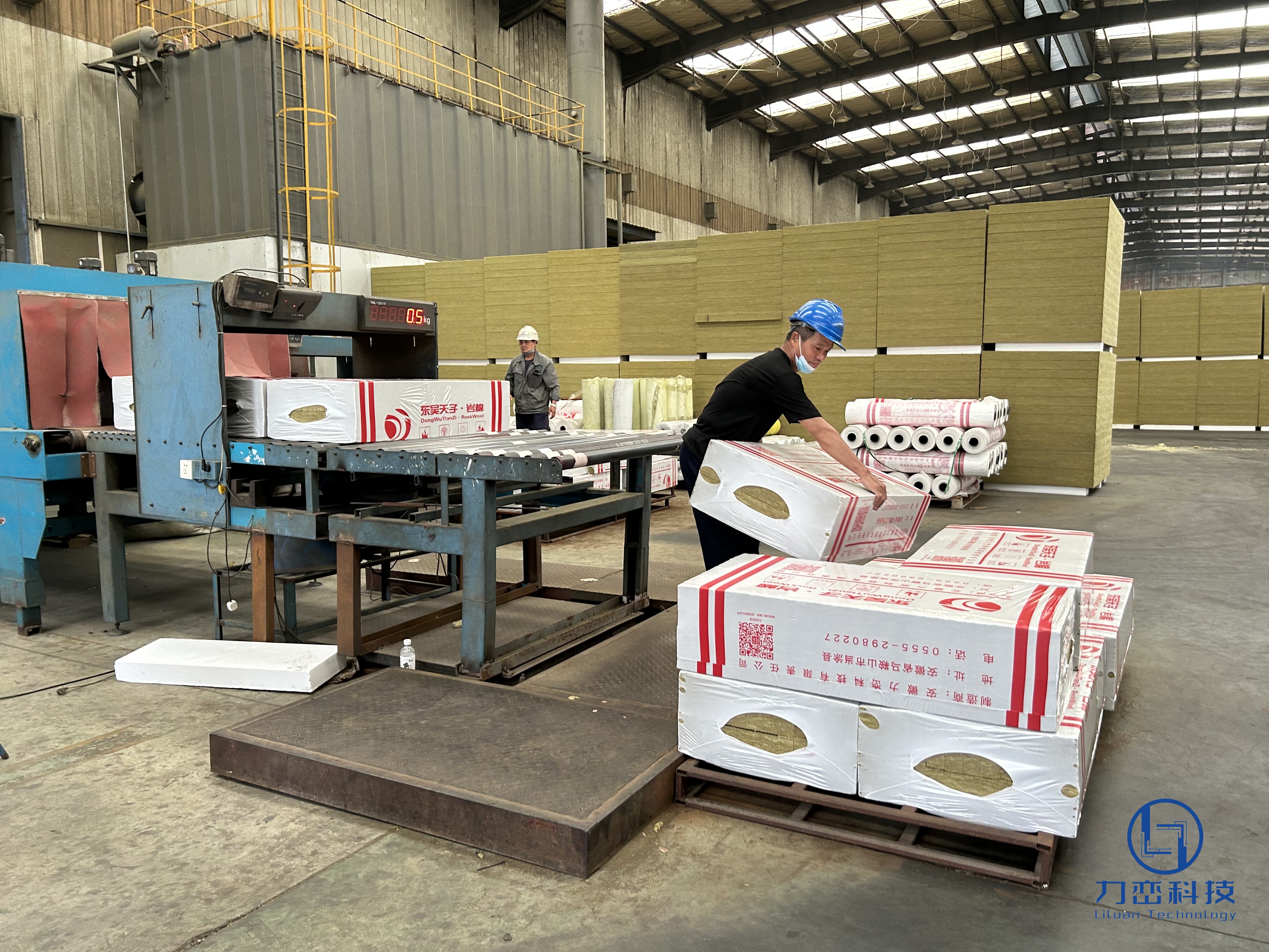 Factory workers lifting and removing finished rock wool boards with Liluan logo packaging from the production line conveyor belt - real manufacturing process at Anhui Liluan Technology