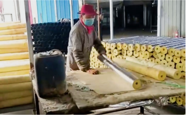 Factory worker wrapping aluminum foil on glass wool pipe section – manufacturing preformed lightweight thermal & acoustic insulation by Liluan Technology