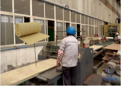 Factory worker handling bare rock wool blanket roll on production line - real manufacturing process for industrial insulation at Liluan Technology