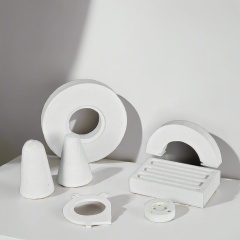 A variety of customized white vacuum-formed ceramic fiber special-shaped parts, including cones, rings, and a grooved block, are arranged for display in a laboratory setting——LiLuan Technology