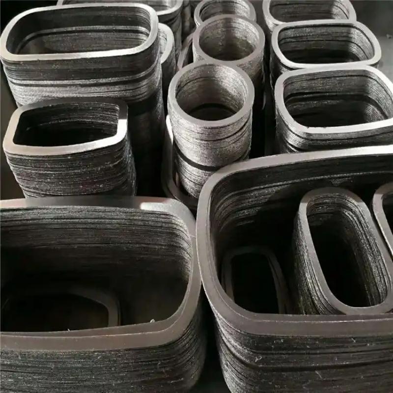 A detailed top-down view of multi-layered stacks of Liluan high-strength composite graphite gaskets. The gaskets are in various nested oval and rectangular shapes on an industrial work surface, ready for installation. The close-up view of the edges reveals the complex alternating layers of graphite and multiple metal reinforcement inserts, illustrating the high-strength multi-layer construction required for non-circular applications like high-pressure valve bonnets.---LiLuan Technology