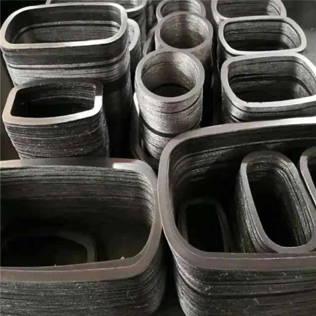 A detailed top-down view of multi-layered stacks of Liluan high-strength composite graphite gaskets. The gaskets are in various nested oval and rectangular shapes on an industrial work surface, ready for installation. The close-up view of the edges reveals the complex alternating layers of graphite and multiple metal reinforcement inserts, illustrating the high-strength multi-layer construction required for non-circular applications like high-pressure valve bonnets.---LiLuan Technology