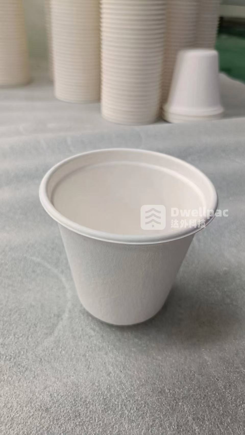 Molded pulp cup sample with a flared rim and stacked cups in the background
