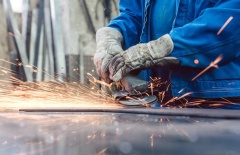 Worker grinding metal with Fuji angle grinder, sparks flying in industrial workshop