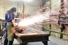 FUJI High-Frequency Angle Grinder with specialized grinding wheel performing heavy-duty weld removal on steel plates in Foundry