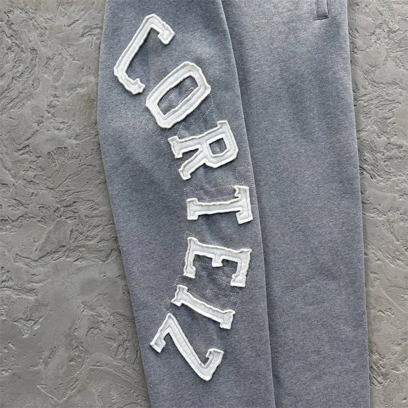 Close view of white vertical lettering on grey Corteiz Lundun Stitch sweatpants