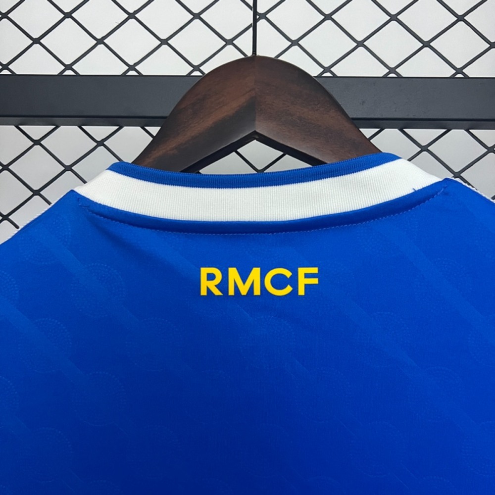 Close-up of the 2025-26 Real Madrid second away fan version jersey showing yellow RMCF lettering on blue fabric near the collar.