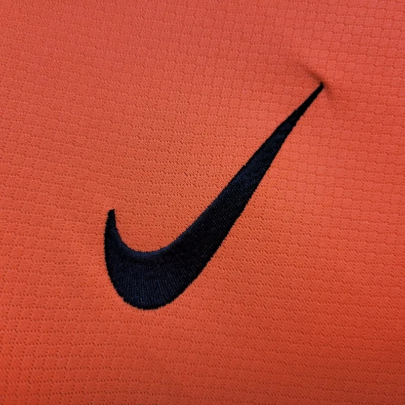 Detailed close-up of the embroidered Nike swoosh logo on the 2025-26 FC Barcelona Second Away Jersey orange fabric.