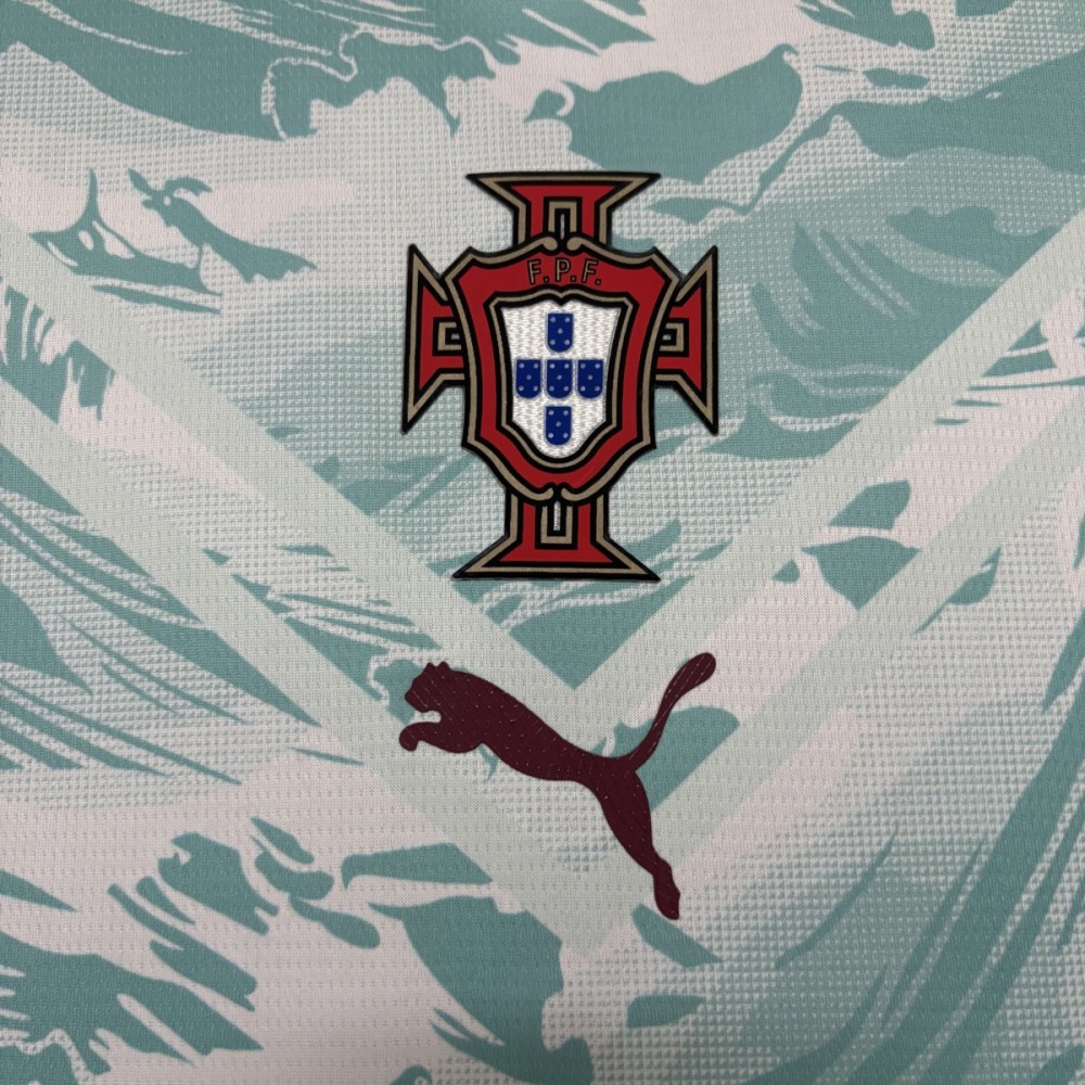 Close-up of the Portugal national team crest (FPF) and burgundy Puma logo on the Portugal 2026 World Cup away jersey with teal ocean‑inspired wave pattern on a white base.