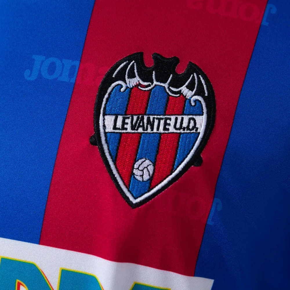 The club crest on the Levante 1999-00 shirt - a shield with a heavy black outline, a black bat with spread wings sitting on top, red-and-blue vertical stripes inside the shield, a white banner across the middle lettered LEVANTE U.D., and a small white football at the bottom point