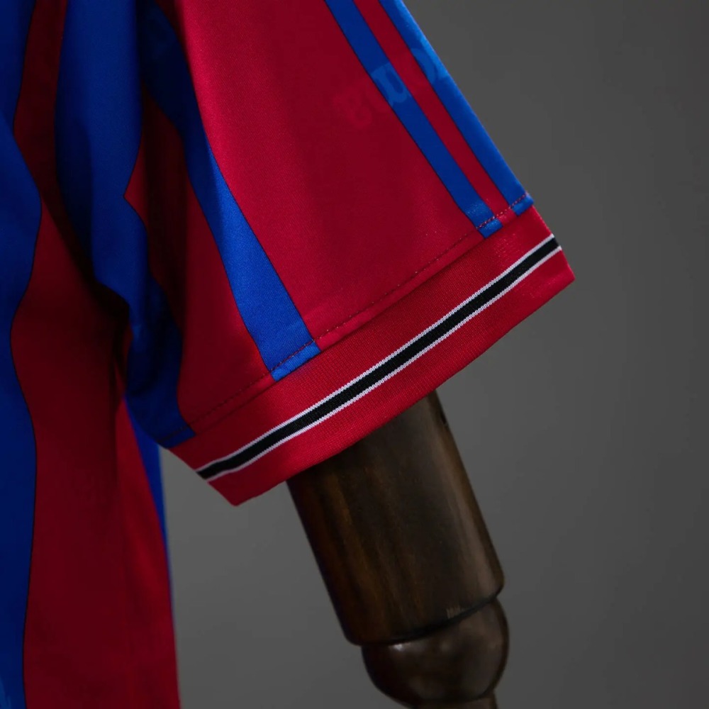 The sleeve cuff of the Levante 1999-00 shirt - crimson fabric with a fine white line, a black line and a second fine white line running along the cuff edge, beside a sleeve panel of finer red and blue pinstripes and a thin white piping line