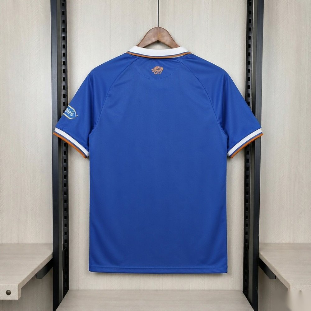 Hull City 2026-27 third shirt back - a solid royal blue body with no pattern, a white fold-over collar with orange edging, a small gold embroidered tiger head centred just below the back of the collar, raglan sleeves with white cuffs banded in blue and orange, a small light-blue shield patch on the wearer's left sleeve, and a completely blank lower back; no name and no number