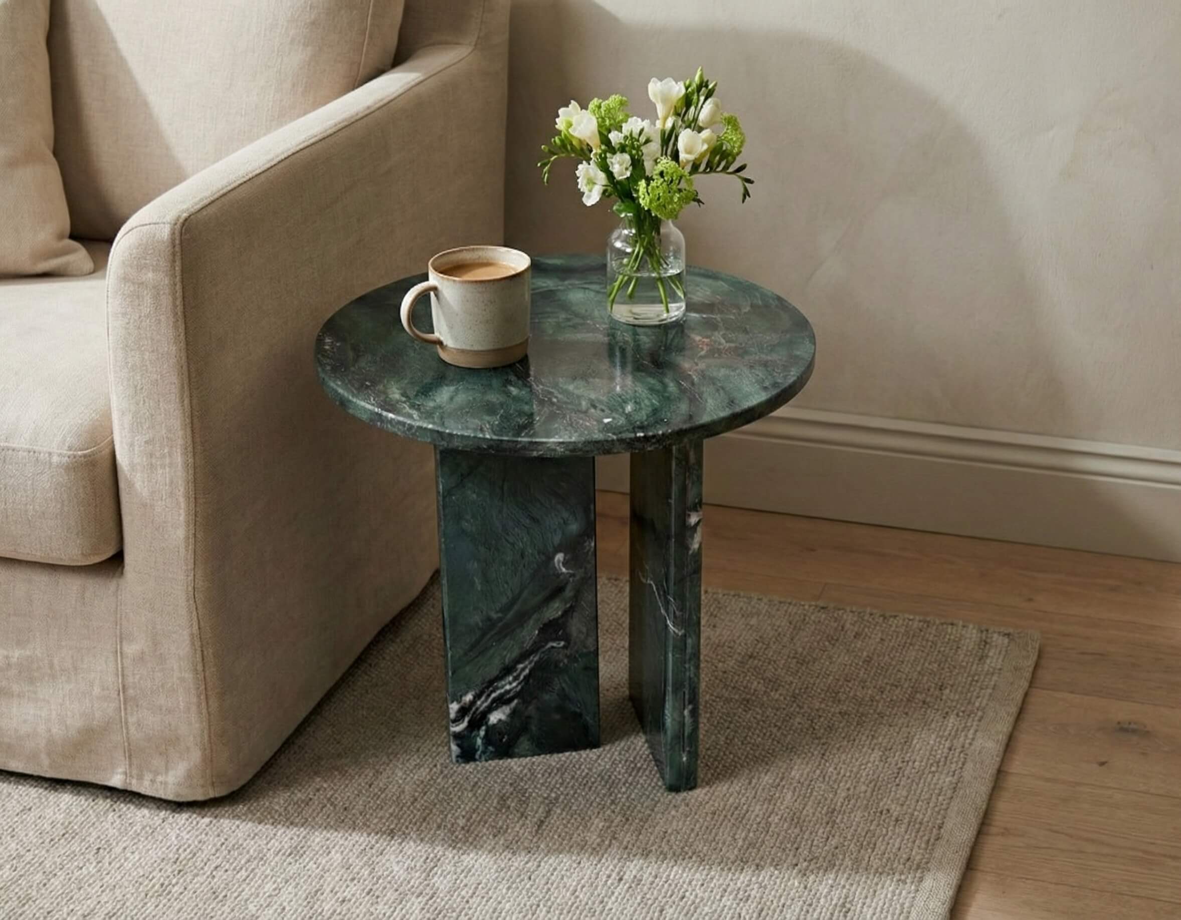 Round green marble side table styled with fresh flowers and coffee next to a beige armchair in a cozy corner.